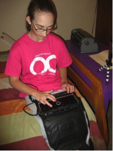 A girl uses a braille notetaker on her bed