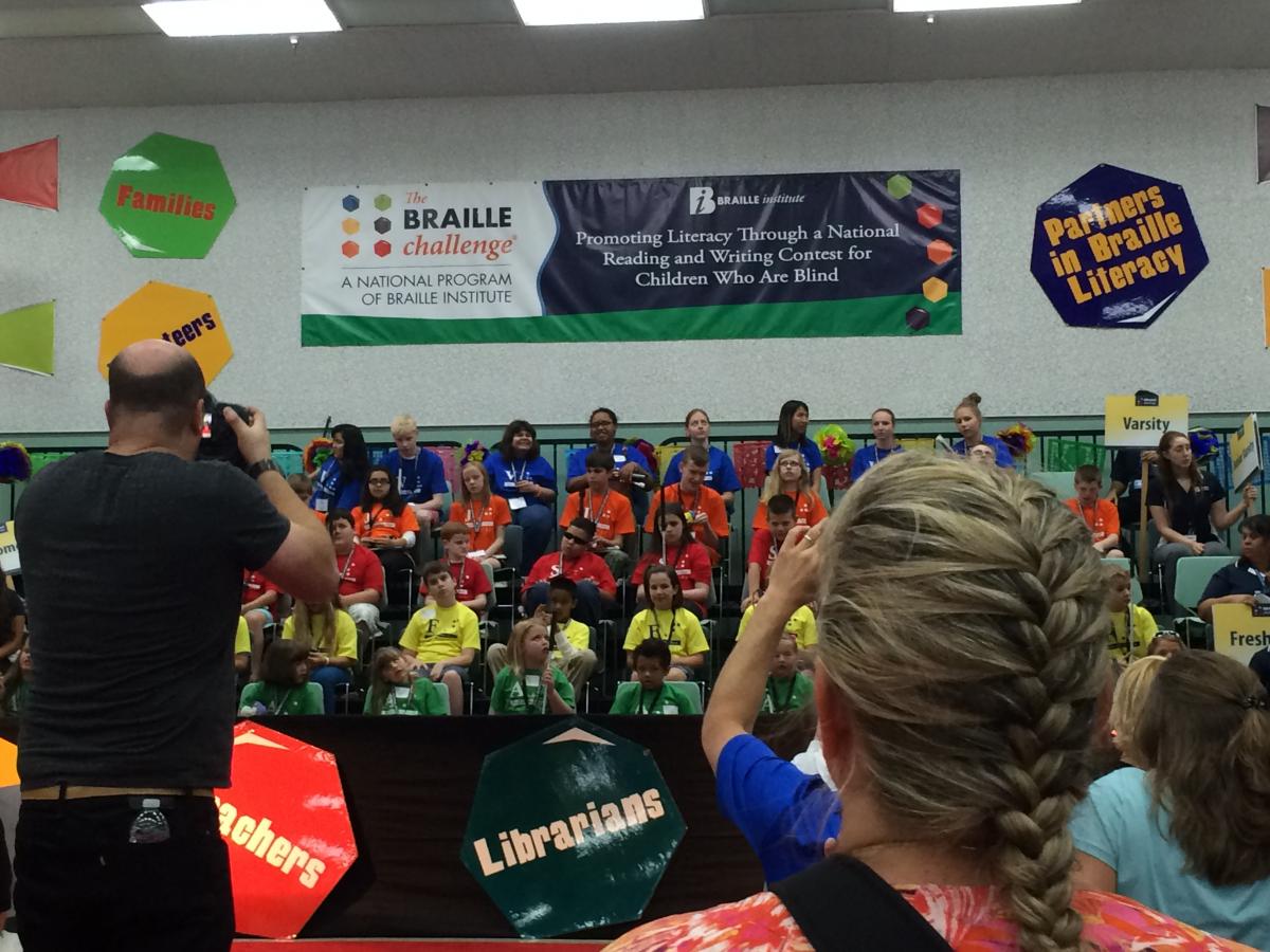 a group of students wearing different colored shirts below a Braille Challenge banner