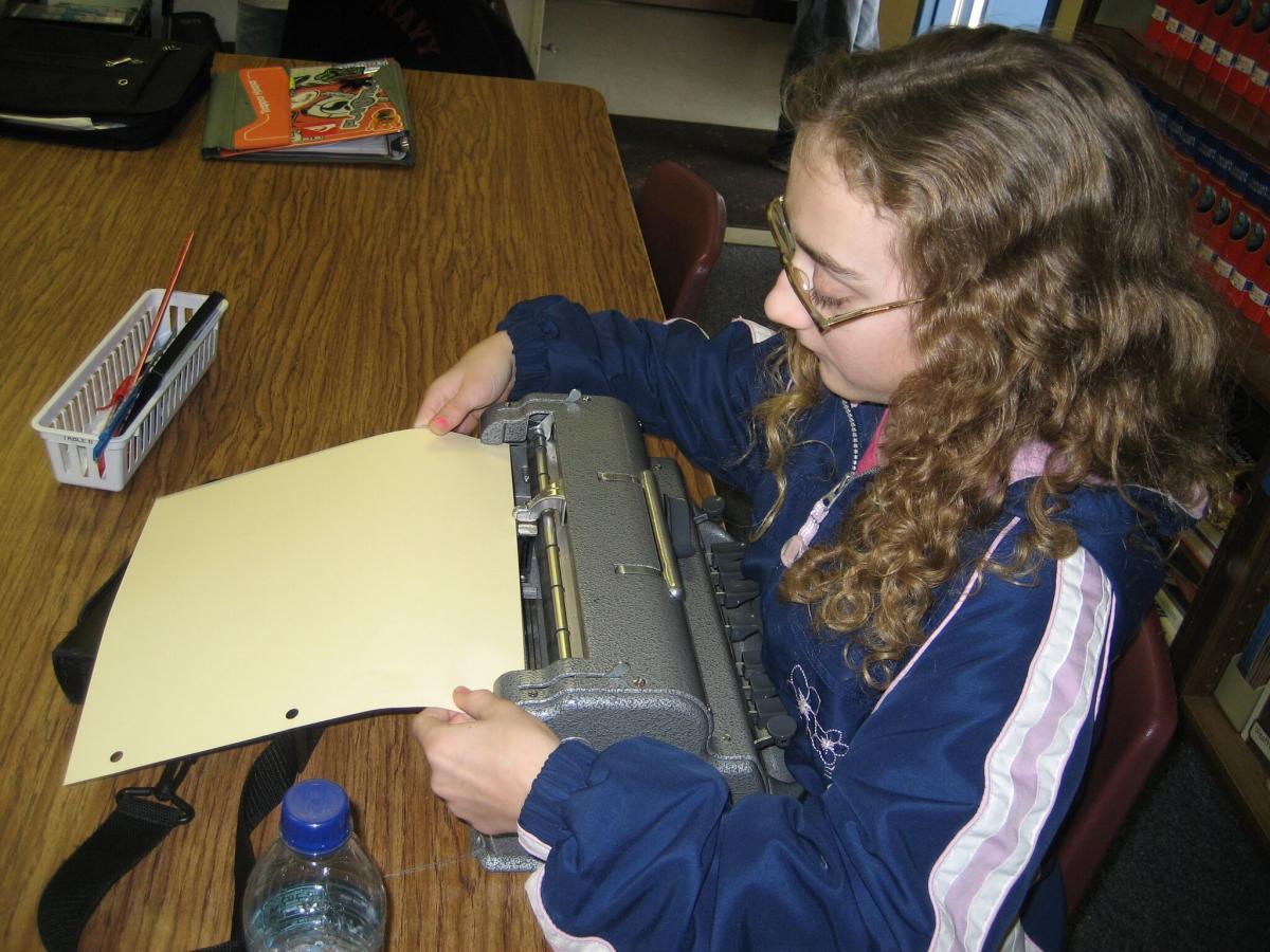 A girl puts paper into her Perkins braillewriter.