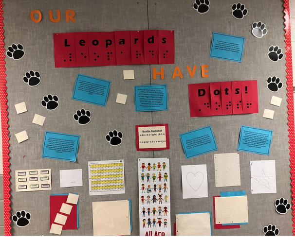 Large school bulletin board that says, “Our Leopards Have Dots!” in print and simbraille.  The bulletin board is covered with print facts about braille and a variety of braille and tactile materials