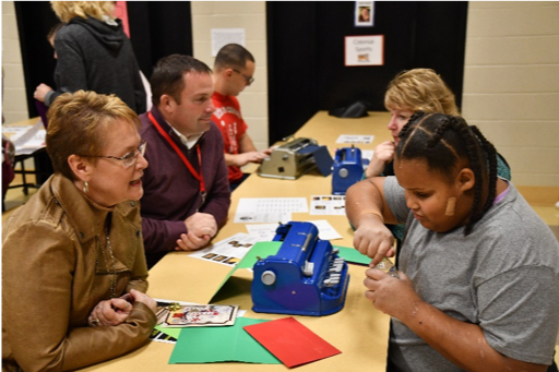 A group of people creating braille cards at a long table