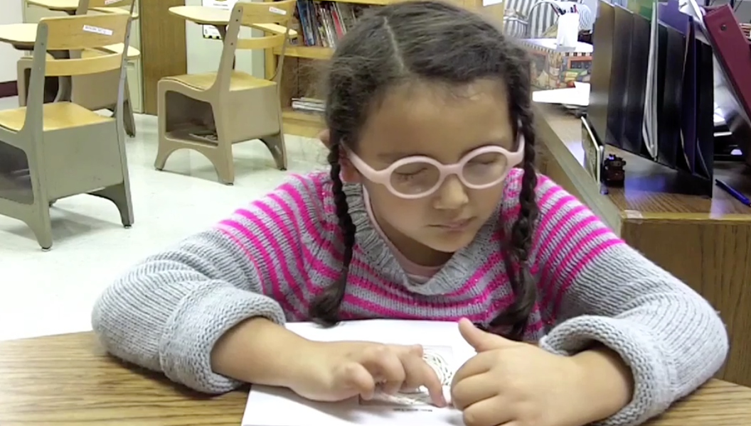 A young girl with glasses reads page of braille.