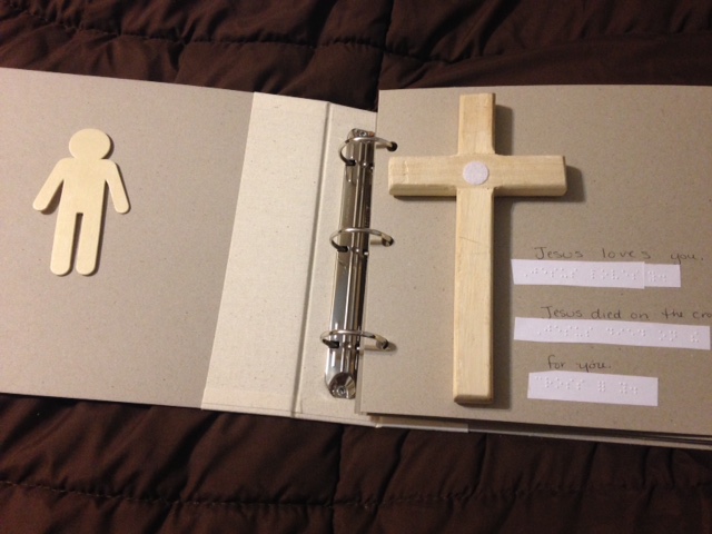 Wooden figure on left page and cross with velcro dot on right page with braille and print text.
