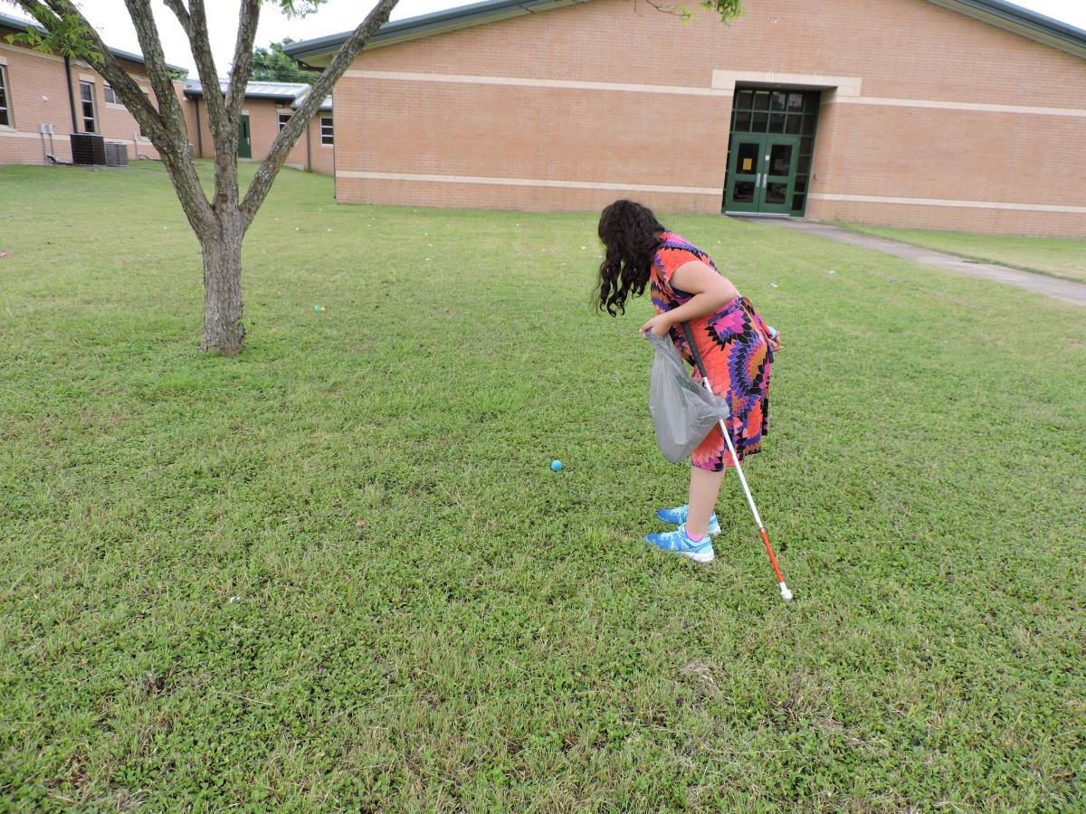 a young girl with a white cane searches for plastic eggs on grass