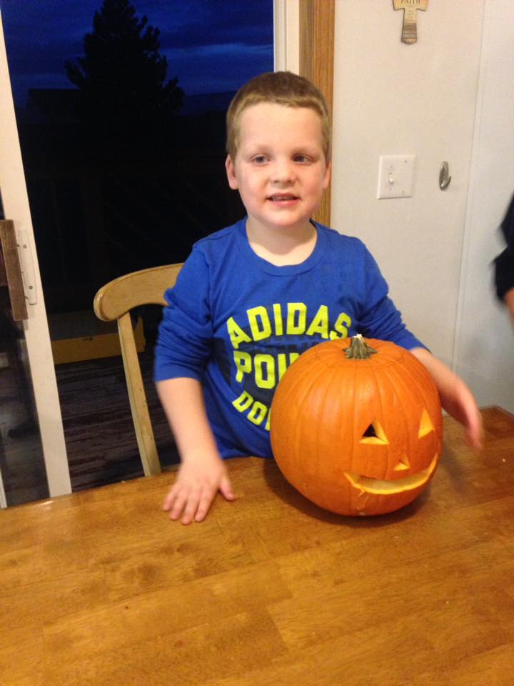 A boy stands next to a carved pumpkin