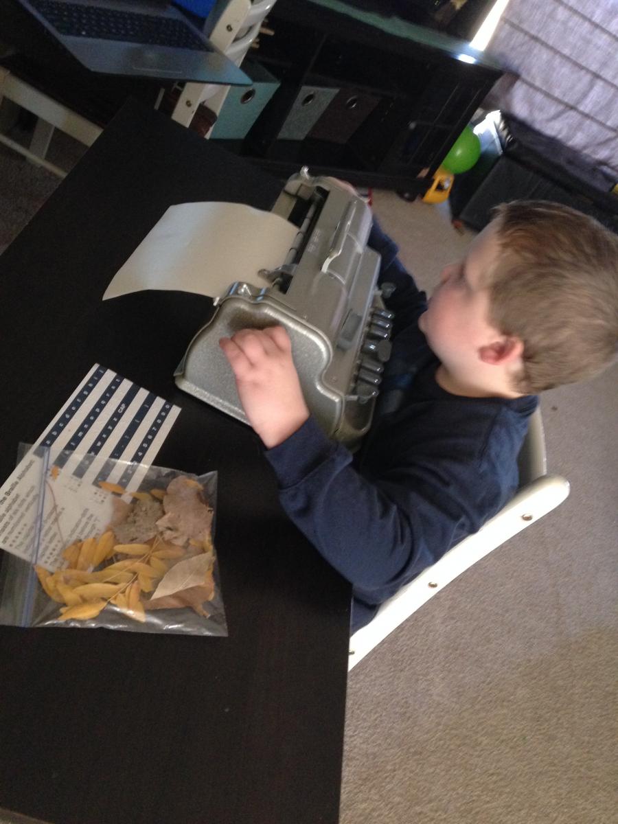 Boy using braille writer with bag of dried leaves