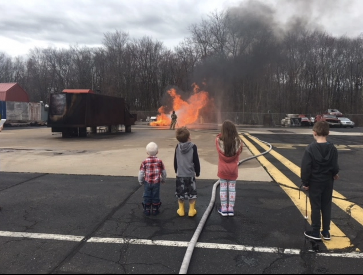 Three young children look on as a fire burns outdoors.