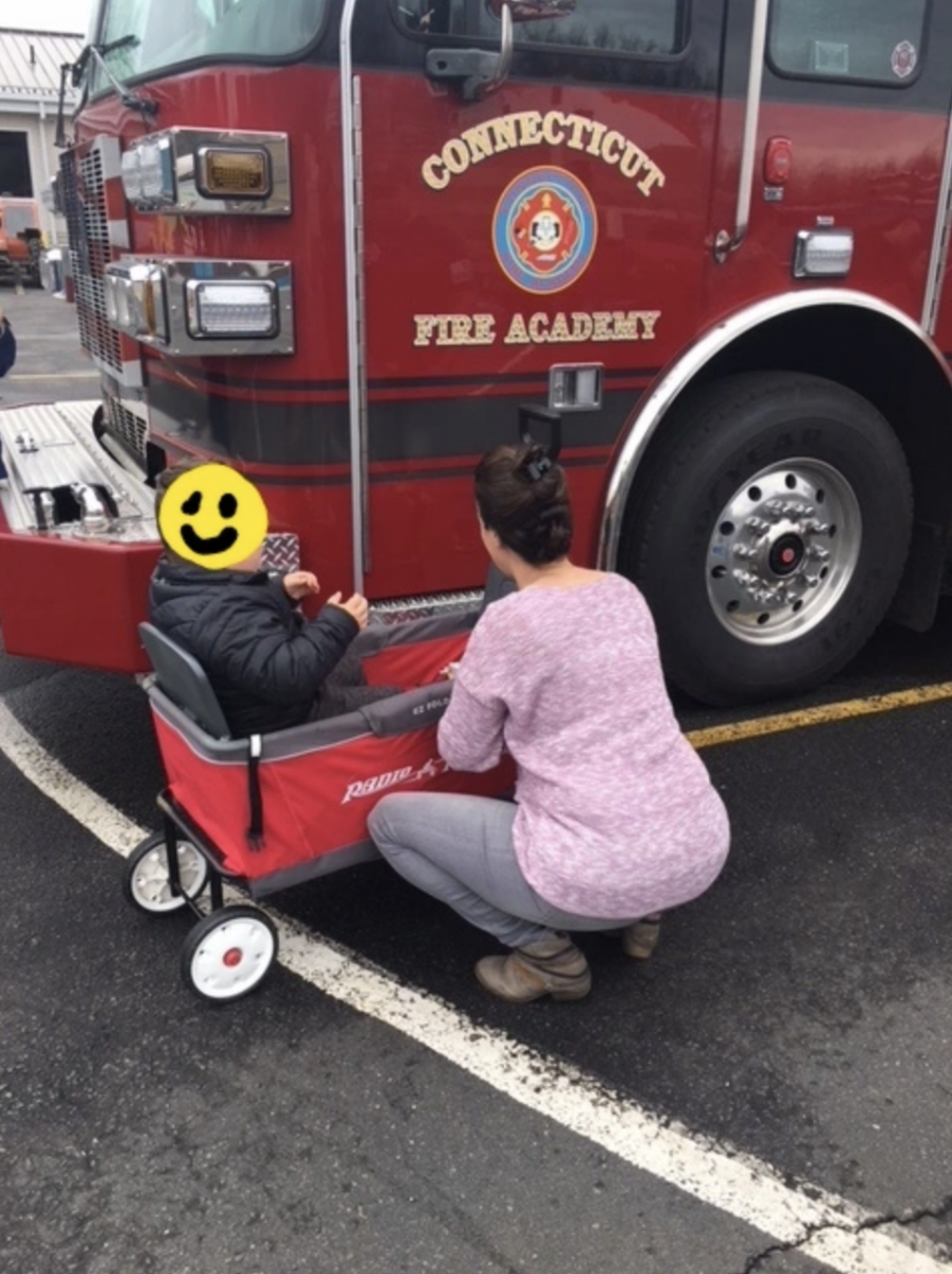 A young child in a wagon examines a fire engine.