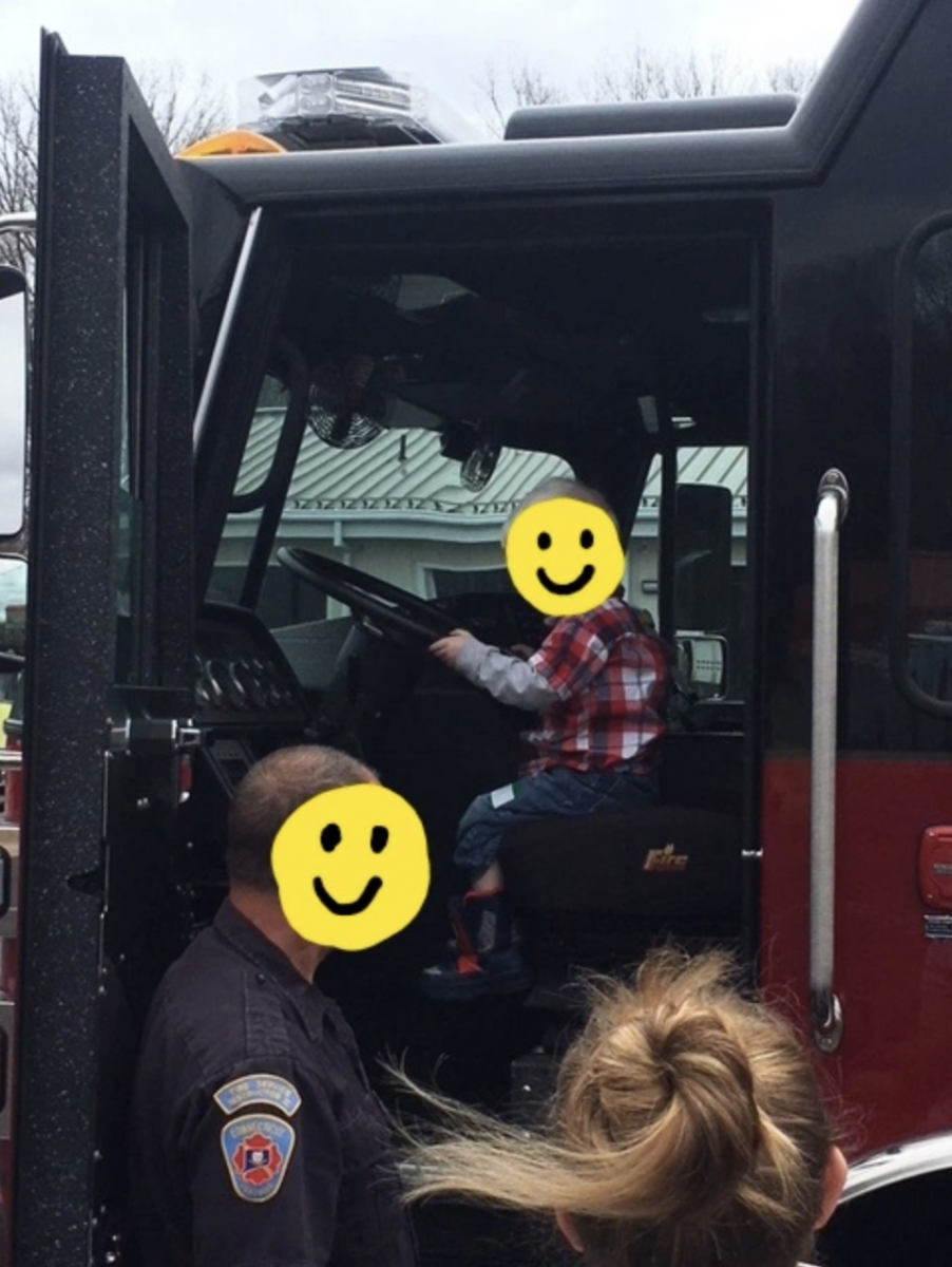 A young boy pretends to drive a fire truck.