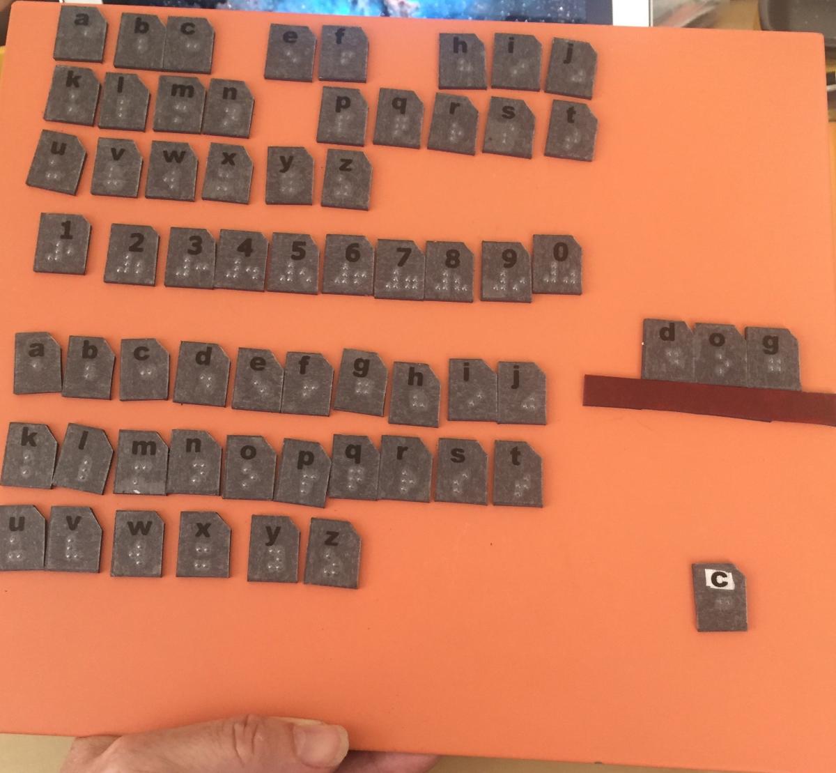 Full set of braille magnetic letters magnet board with two sets of alphabet and number 0-9 and the word dog positioned above long red rectangle
