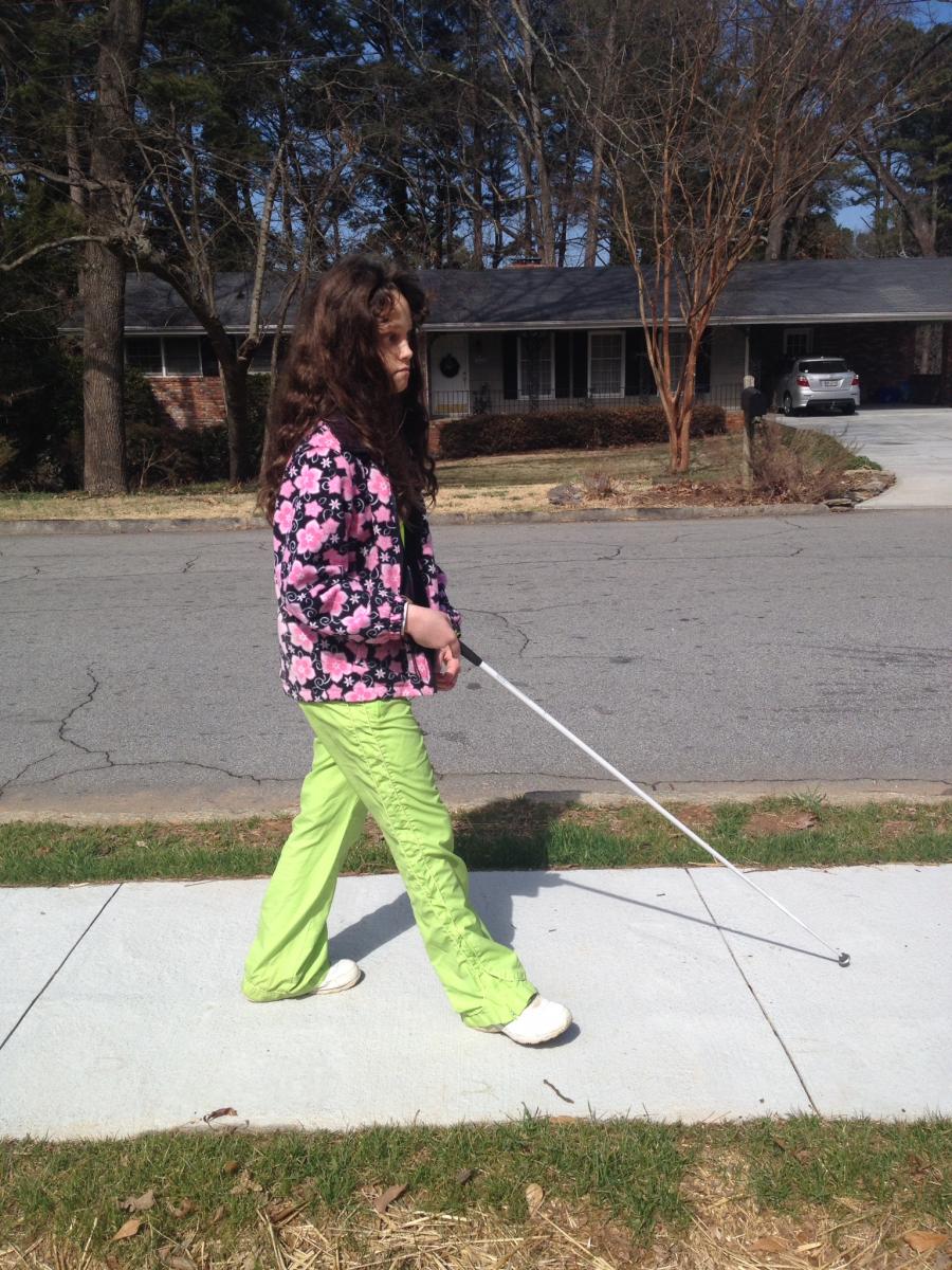 Girl traveling with cane outside on sidewalk