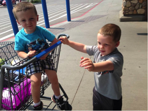 Big brother pushing shopping cart with younger brother riding in it