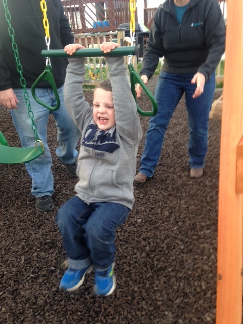 A boy hangs from a bar on a playset