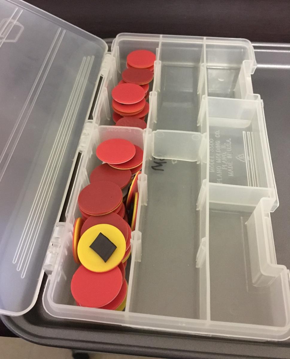 a plastic container with plastic counters with magnetic tape on the back of them