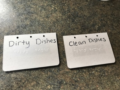 two cards next to each other, one says dirty dishes and the other says clean dishes in both text and braille