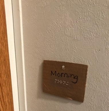 a card hanging on a wall that says morning in print and braille 