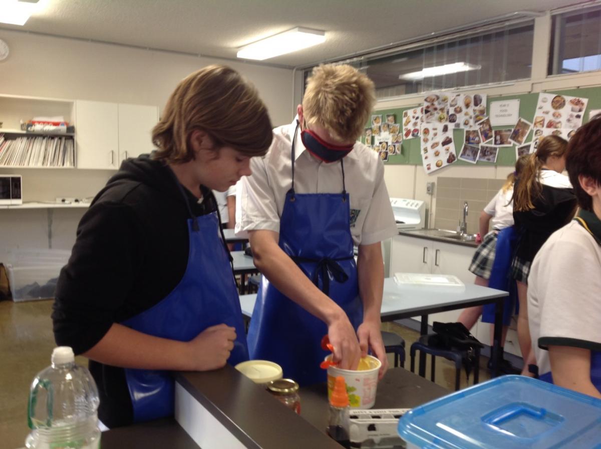 two students, one is blindfolded, work together to measure ingredients for their recipe