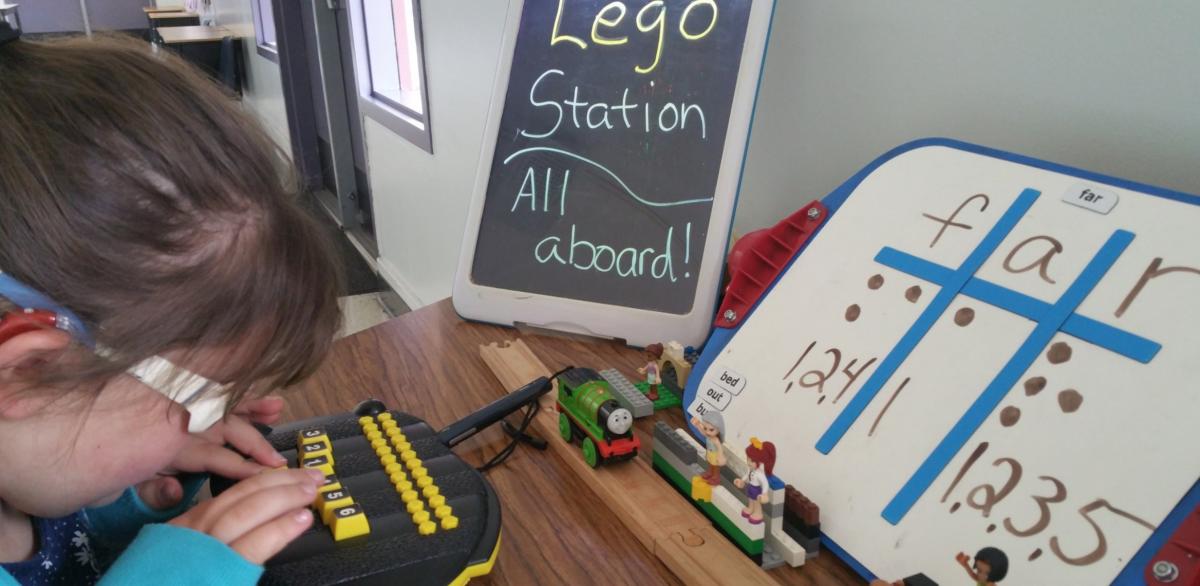 The Lego Girls cheer on Percy the train as he rolls down the track.  Using APH’s “All Aboard the Sight Word Express,” All-in-One Board, and BrailleBuzz at Lego Station.  Dual media lesson with a goal of in-putting words correctly into BrailleBuzz.  A lighted marquee says “Lego Station all aboard!!”