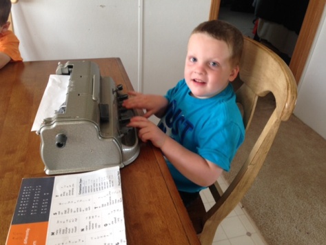 Liam sitting at a table writing with his brailler. Liam writing with his brailler at a table