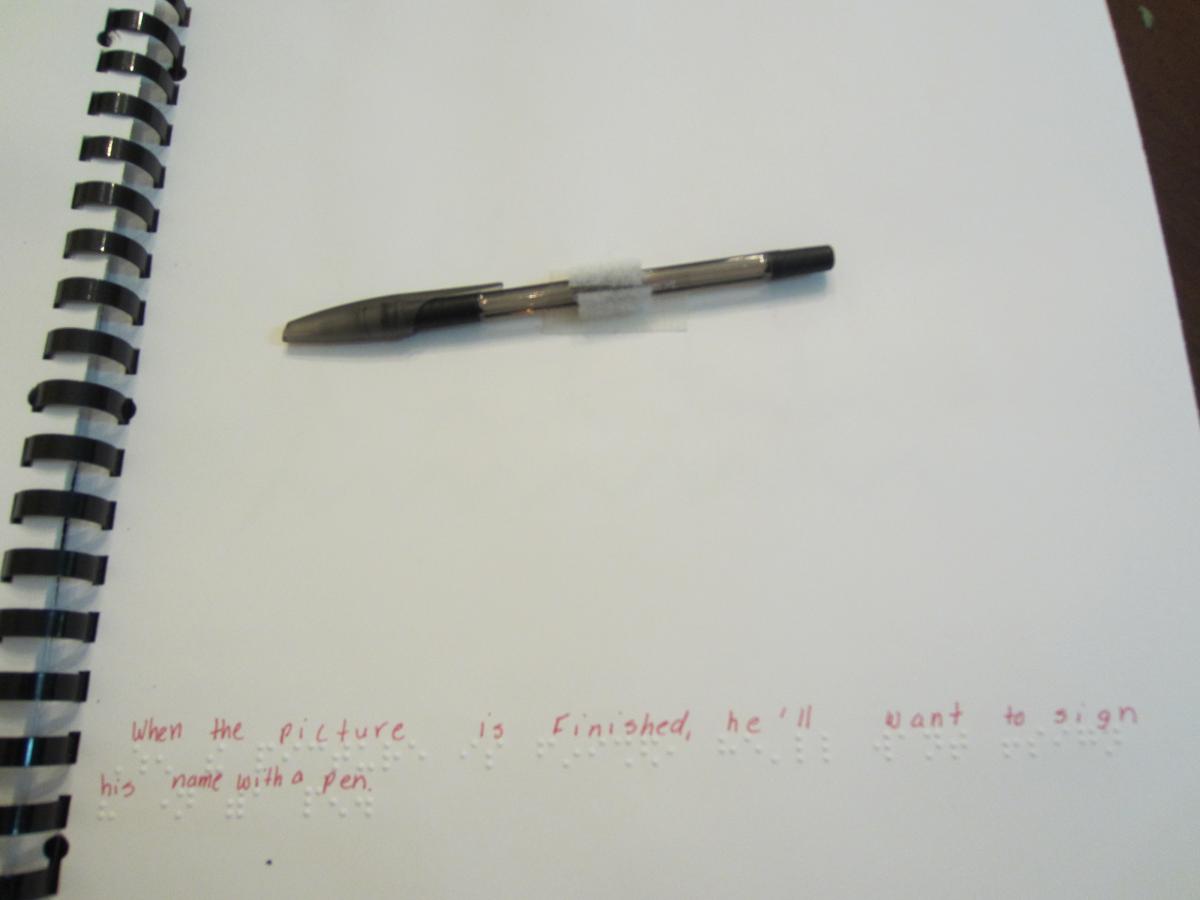 a pen attached to a page with velcro with braille text