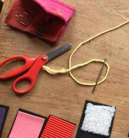 a needle threaded with yellow yarn, a pair of scissors, and supplies to make tactile labels for the baskets