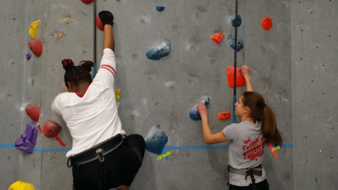Two teenage girls climb a rock wall.