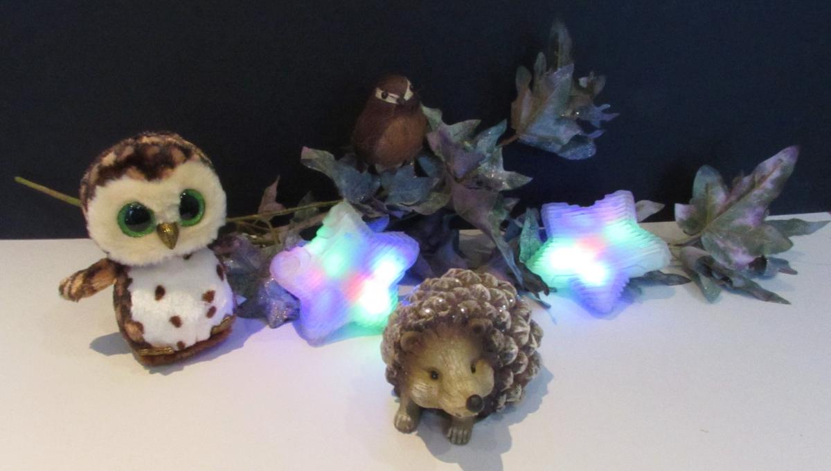 a toy owl and hedgehog among pine cones and star lights