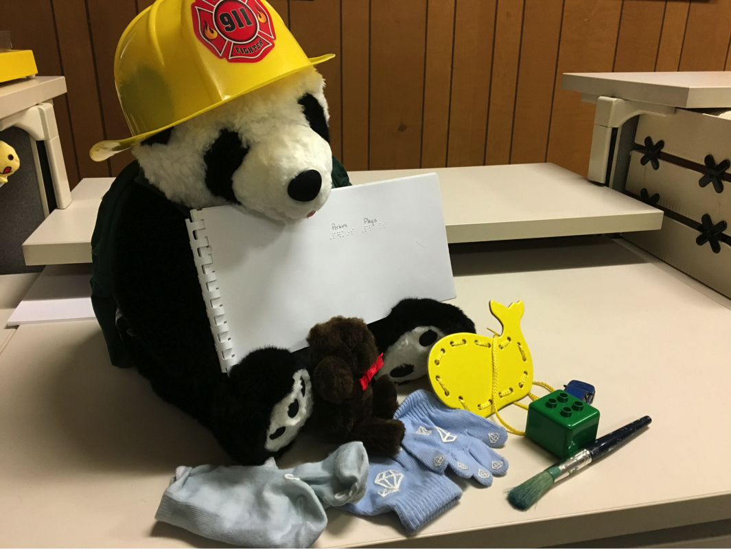 Perkins with fireman hat, socks and mittens, stuffed bear, lego, paintbrush, lacing card.