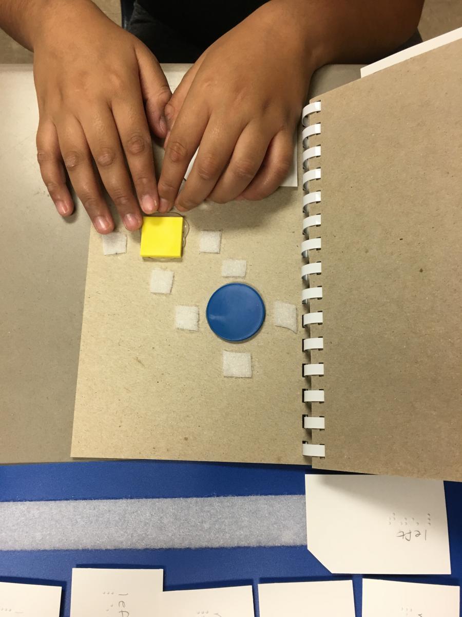 Student reading braille word on page with circle and square Student reading braille word