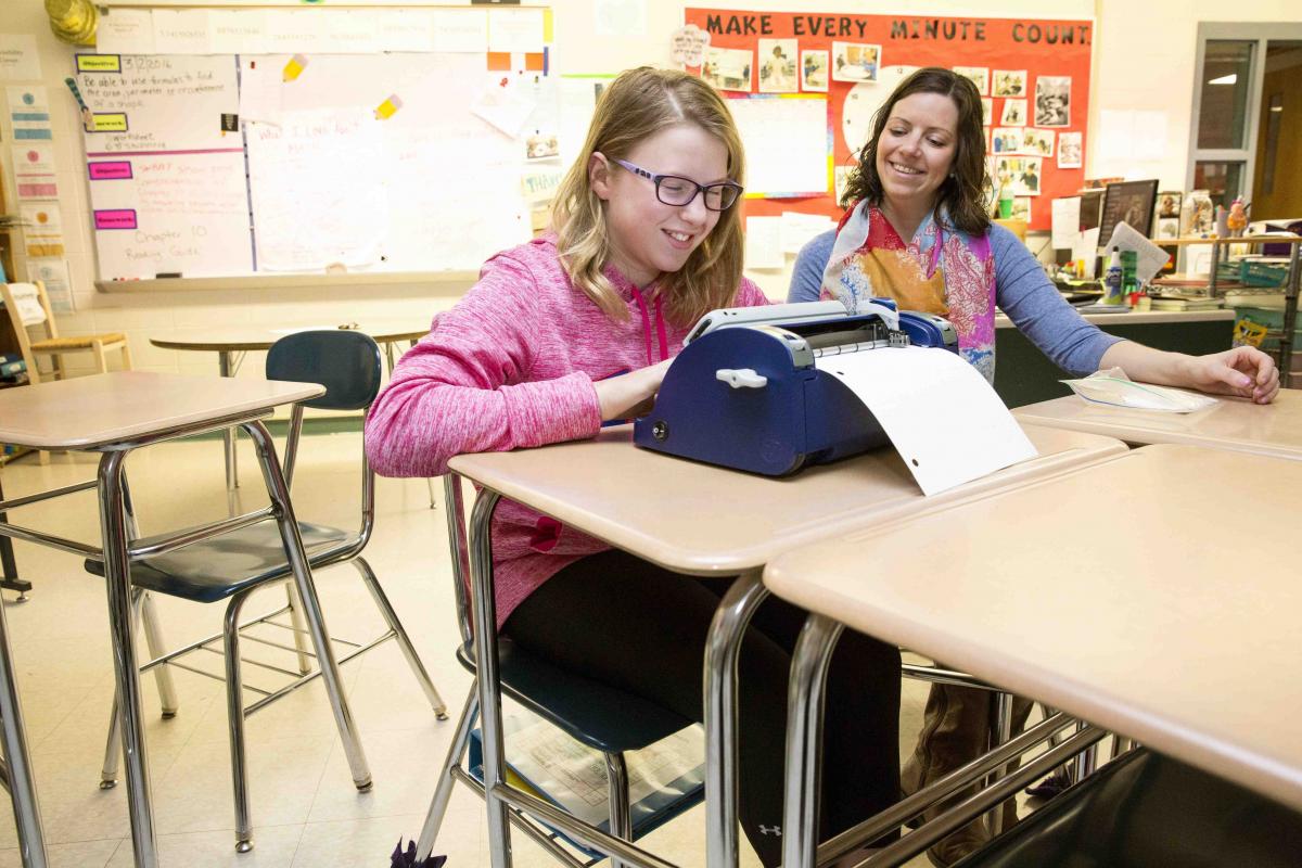 A girl with glasses uses a SMART Brailler in a regular ed classroom.