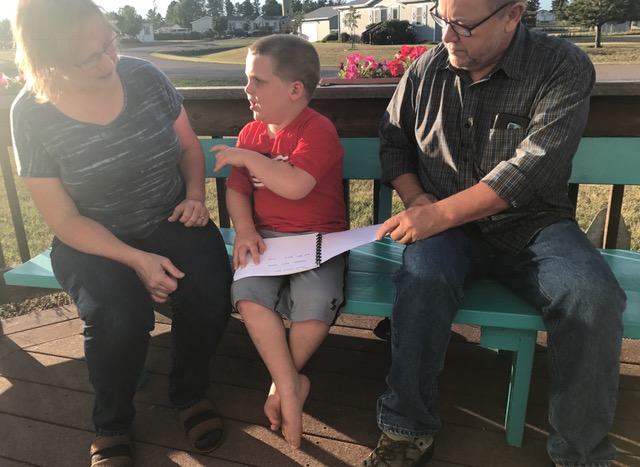 Reading book with his grandparents and signing what's on the page.