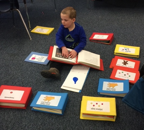 A young boy reads braille books on the floor