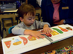 A student uses his hands to explore a board book with his teacher.