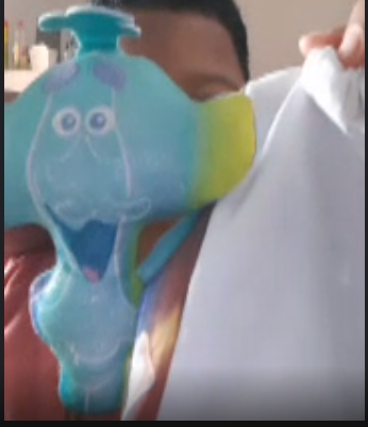 A student holds up a white fabric bag and a blue plush doll.