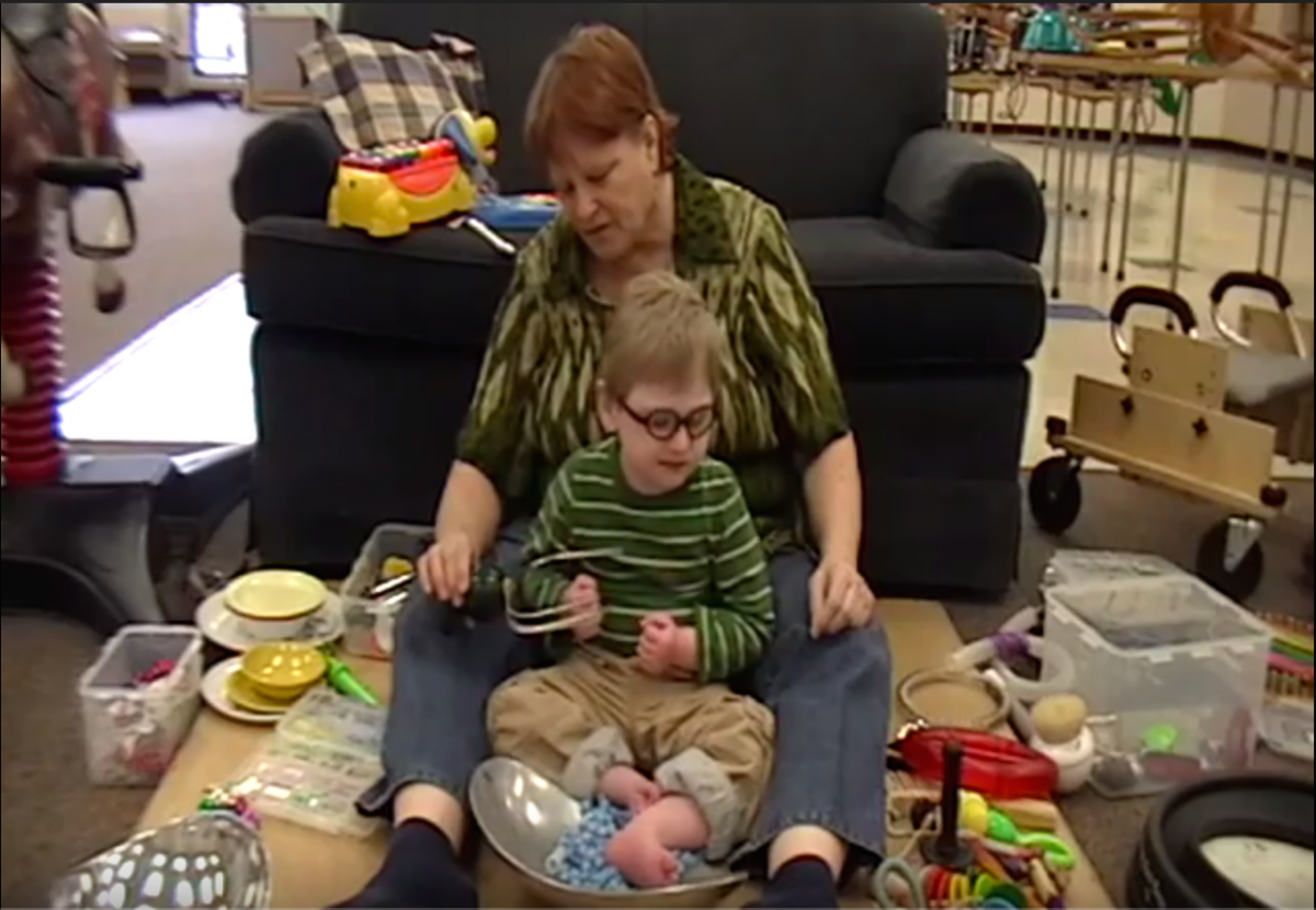An adult sits with a child on a resonance board.