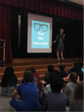Author Shelly Brown stands on stage in front of students in front of a slideshow that says, “See The Awesome.”