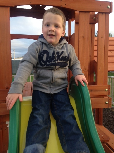 A boy sits at the top of a slide.
