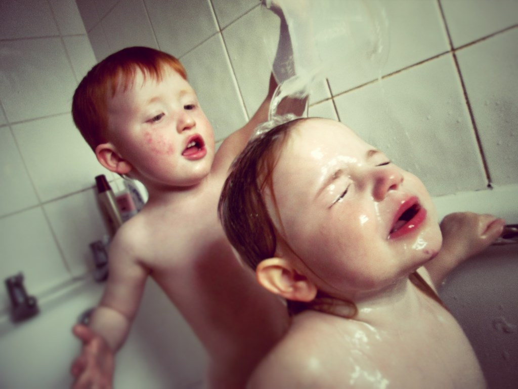 young boy helps wash his sister's hair