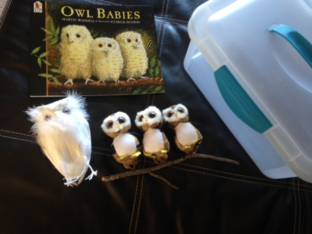 a larger toy owl with three small toy owls and a copy of Owl Babies book