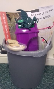 a bucket with a toy dragon, a book, and other items related to the dragon theme