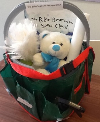 a bucket with a plush white bear, a plush white puff, and a book