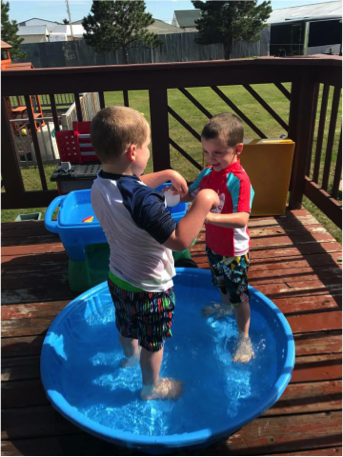 Two boys hold hands while standing in a wading pool