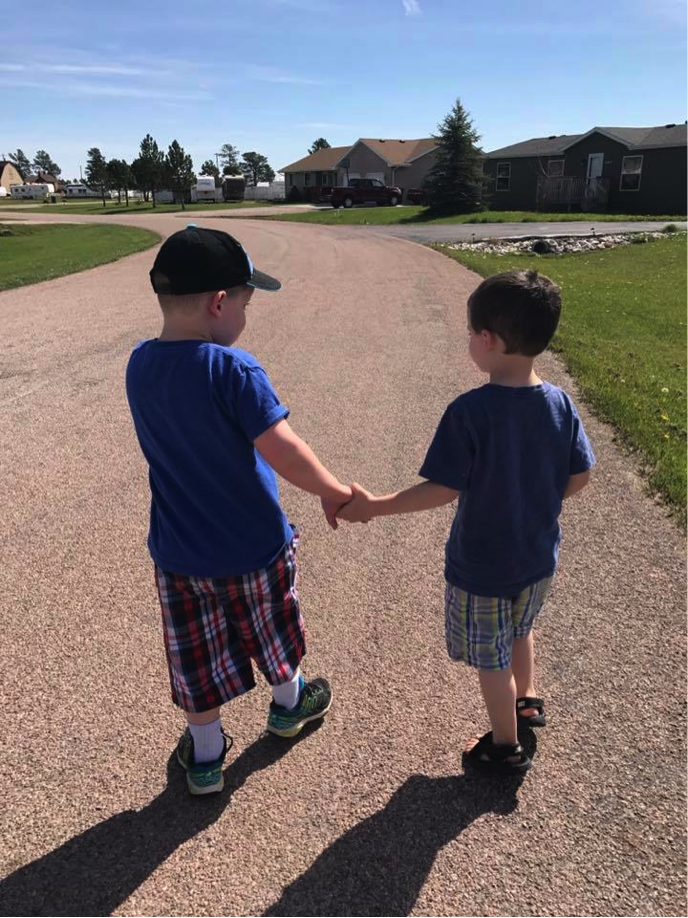 Two boys holding hands as they walk down the road