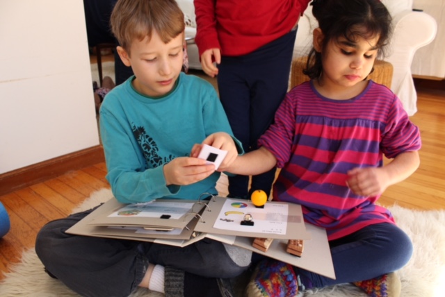 two children sitting on the floor with the tactile book, they are handling tactile objects that are velcroed in to the book