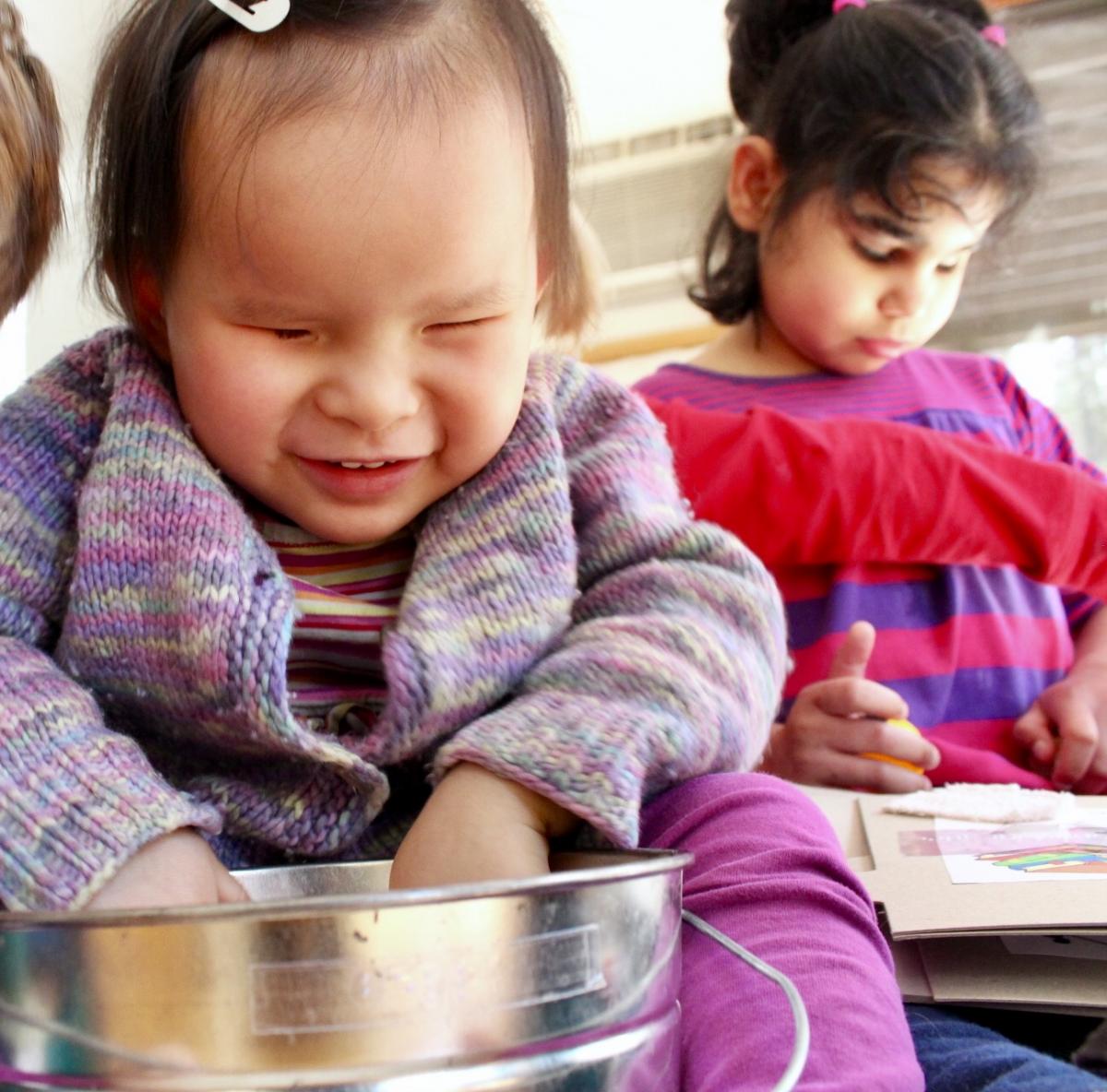 A young girl smiles as she explores tactile items.