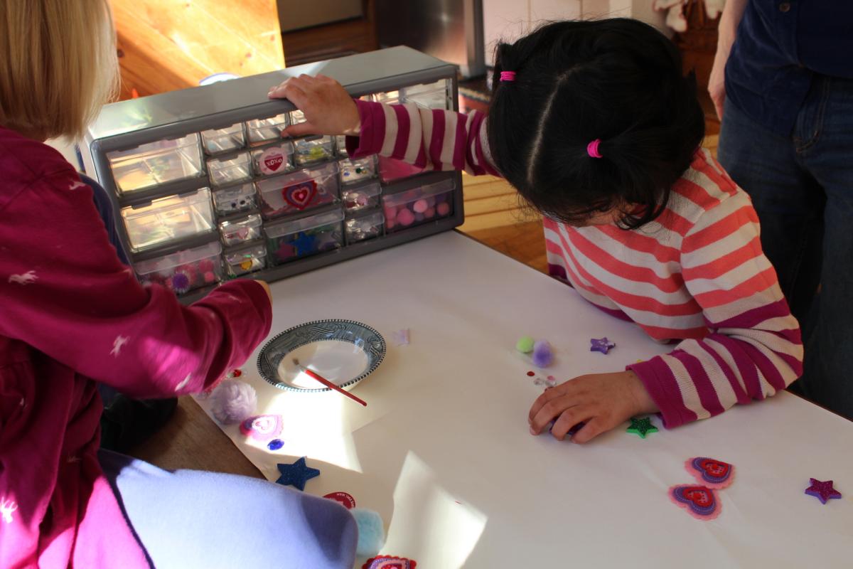 a young girl feels the labels on a set of plastic table top drawers containing arts and crafts supplies