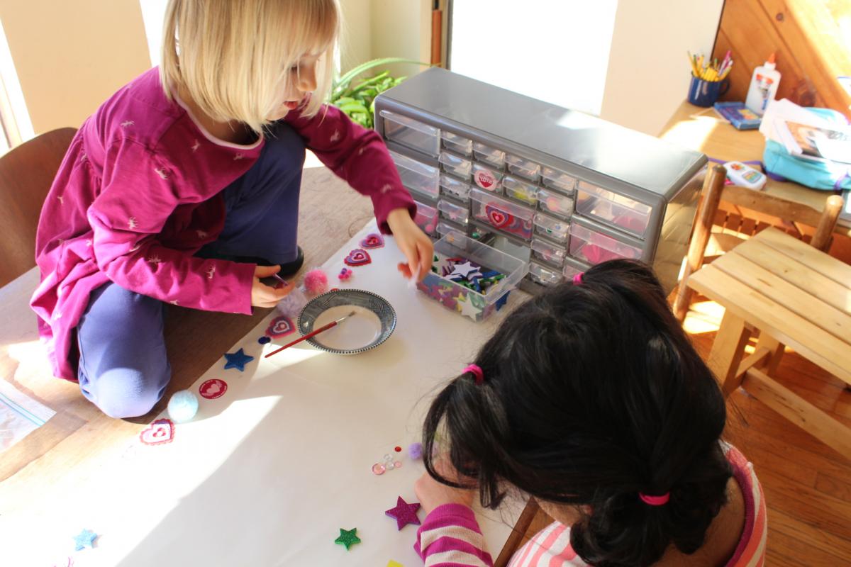 two young girls playing with arts and crafts materials, one of the girls is sitting on the table