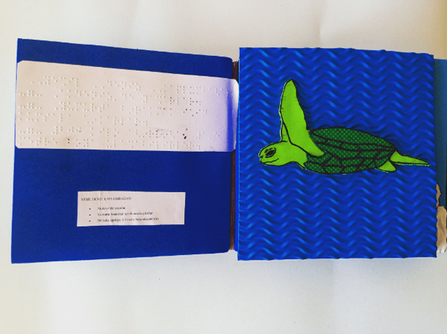 a sea turtle made out of differently textured materials, facing a page of braille description
