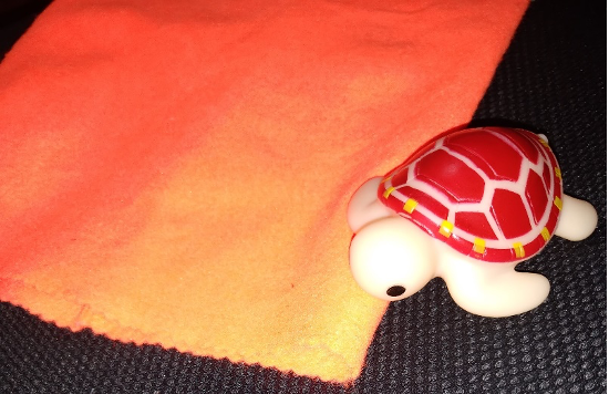 an orange fabric bag and a rubber tortoise, with a beige body and brown shell. The bag and the turtle are on top of a black fabric.