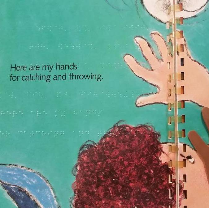 A page from a picture book has braille text added and two sandpaper hands illustrating the text about hands.